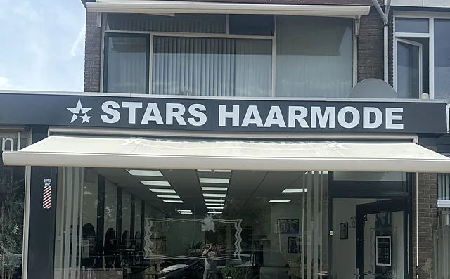 De winkel met het bord STARS HAARMODE, de luifel en de kapperspaal